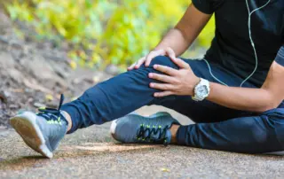 male runner sits on ground holding knee in pain